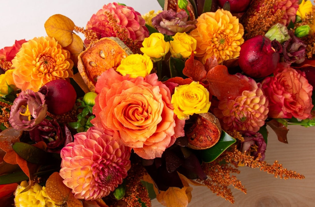 Long, low autumn centerpiece with garden roses and dahlias on a Thanksgiving table.